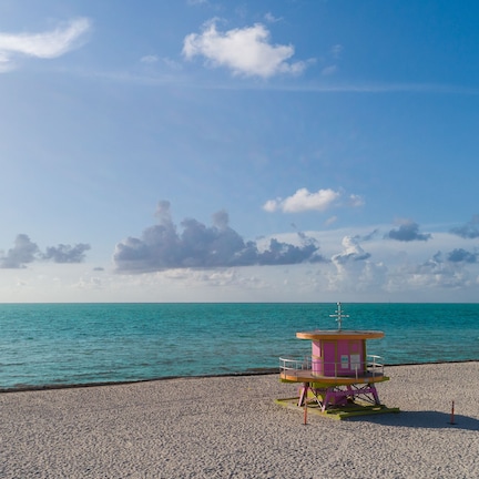 A lifeguard tower on a pebbled beach with clear turquoise water and a partly cloudy sky.