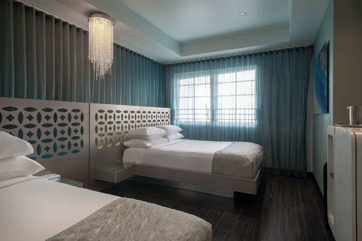 A hotel room with two beds, a chandelier, a large window with curtains, and a modern design.