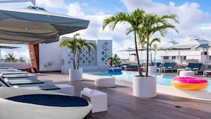 A poolside area with lounge chairs, a floating pool, and potted palm trees.