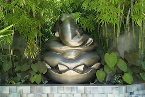 A large, metallic sculpture of an elephant surrounded by lush greenery.