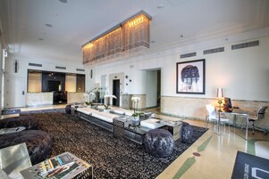 A spacious lobby with a high ceiling, a central seating area with sofas and a coffee table, and a reception desk with chairs.