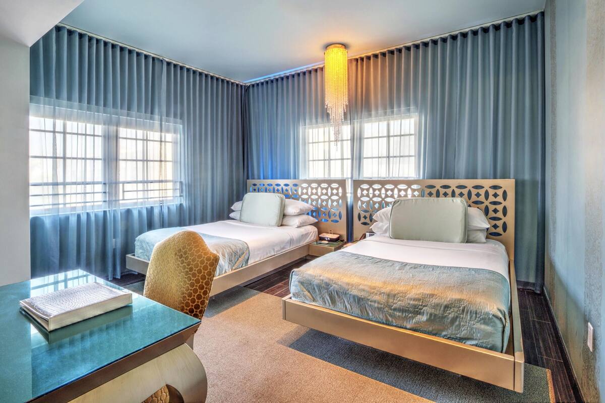 A hotel room with two beds, a desk, and a chair.