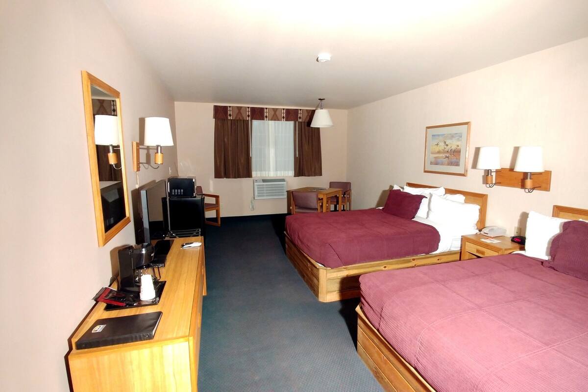 A hotel room with two beds, a desk with a computer, a chair, a small table, and a window with curtains.
