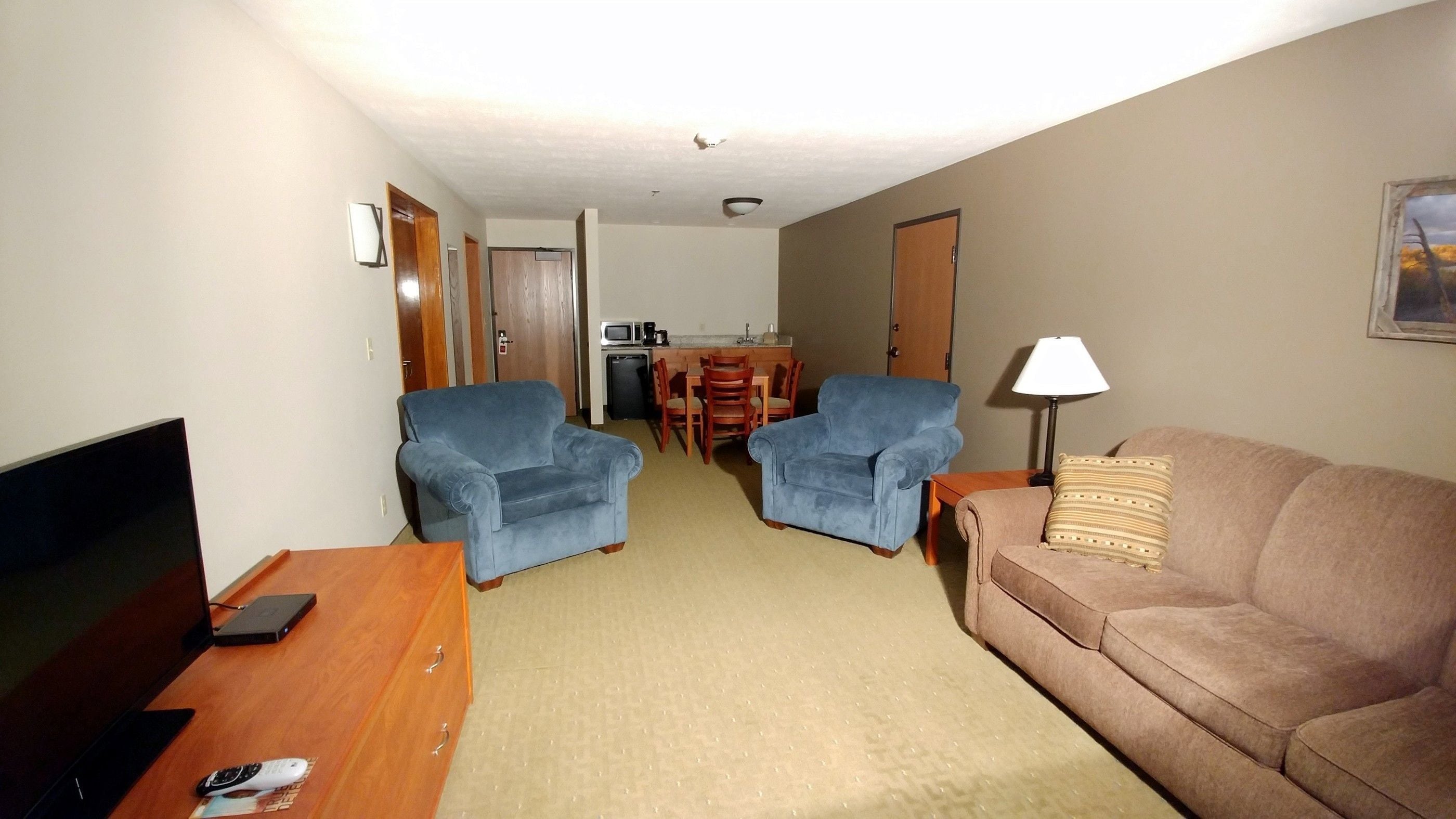 A living room with a TV, two blue armchairs, a brown sofa, and a dining area with a table and chairs.