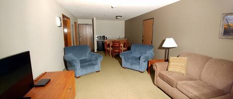 A living room with a TV, two blue armchairs, a brown sofa, and a dining area with a table and chairs.
