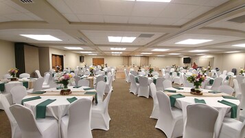 A conference room with rows of tables and chairs, each table adorned with a green table runner and floral centerpieces.