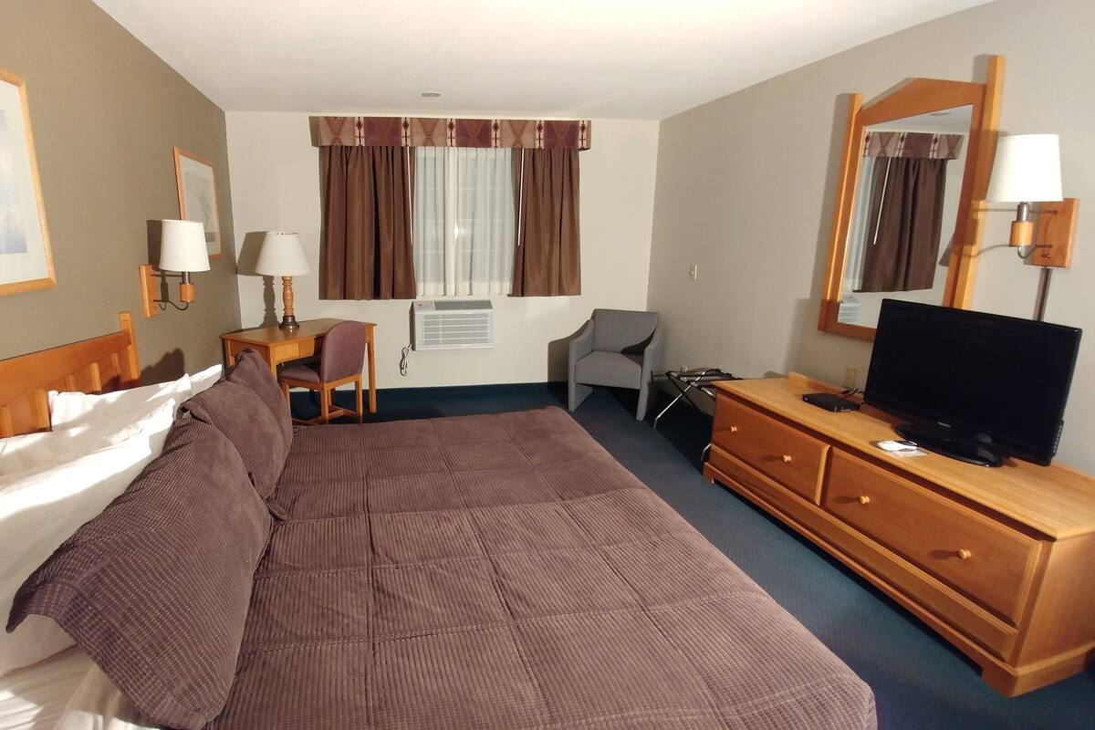 A hotel room with a large bed, a desk with a chair, a television, and a window with curtains.