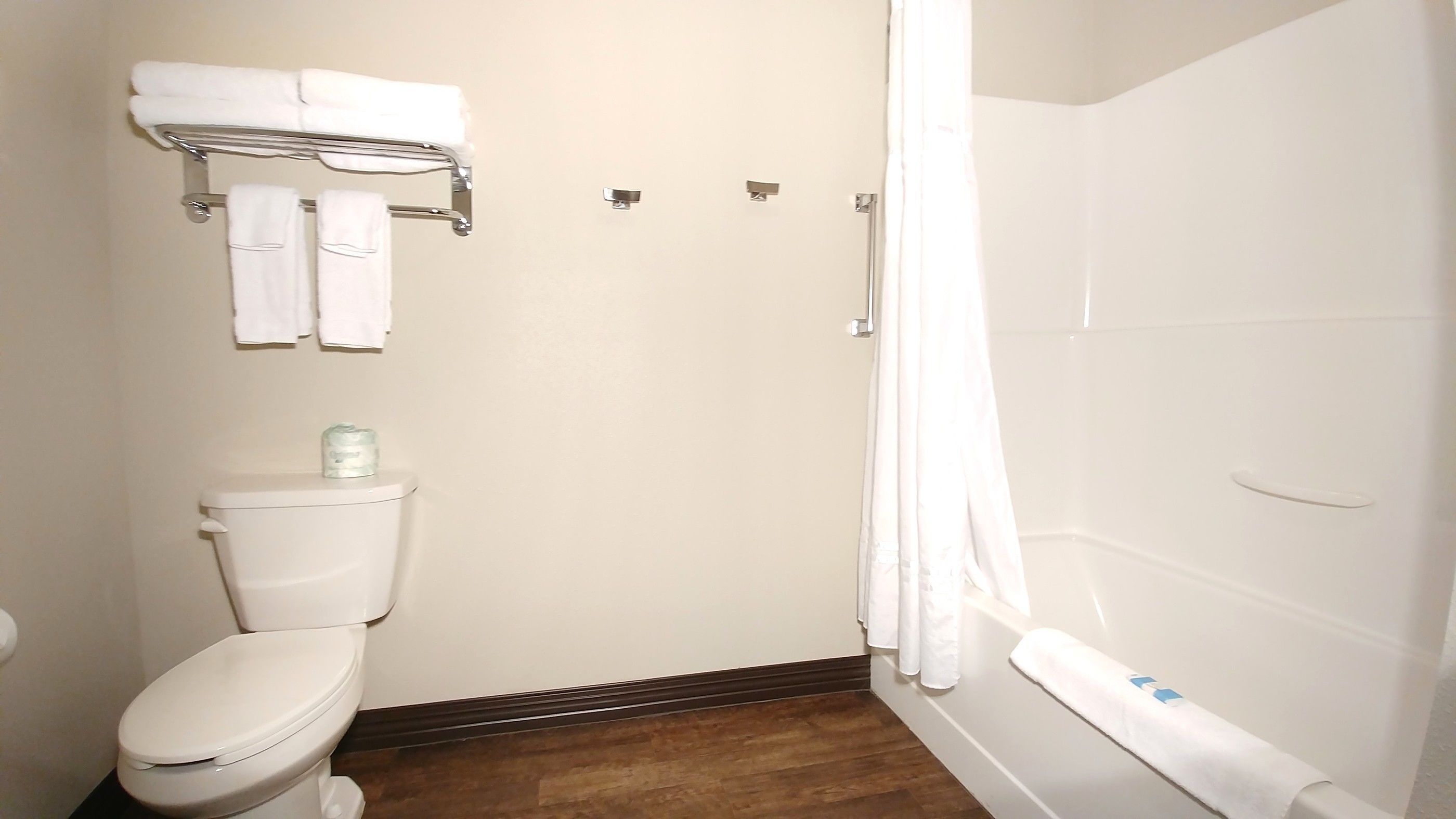 A bathroom with a toilet, a shower with a curtain, and a towel rack with towels.
