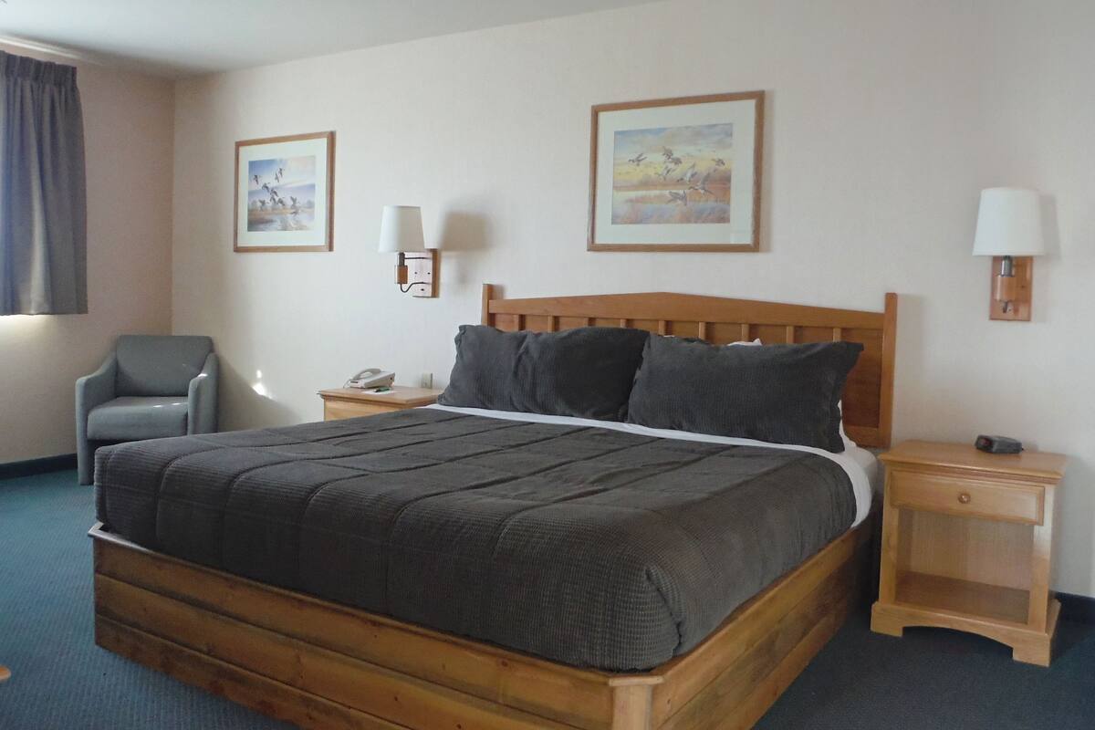 A hotel room with a wooden bed, two bedside tables, a chair, and two wall-mounted lamps.