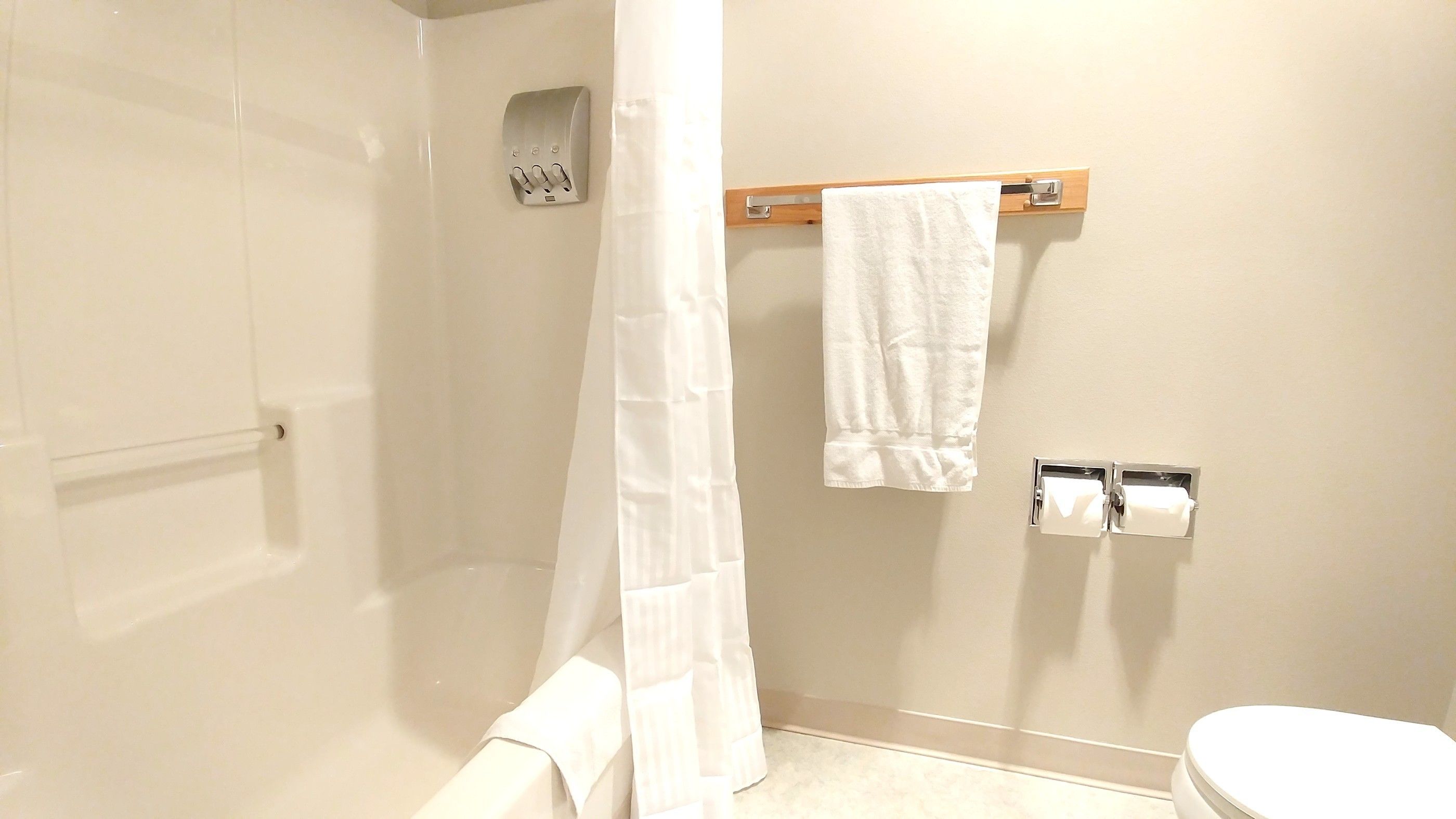 A bathroom with a glass shower enclosure, a white towel hanging on a rack, and a toilet with a paper towel dispenser.