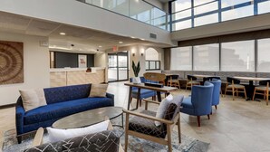 A spacious lobby with a blue sofa, round coffee table, and blue chairs. There is a reception desk and a seating area with a high ceiling and large windows. - Drury Inn & Suites St. Louis St. Peters (St. Peters)