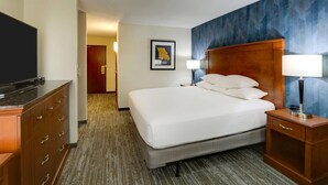 A hotel room with a bed, a dresser, a nightstand with a lamp, a framed map on the wall, and a carpeted floor. - Drury Inn & Suites St. Louis St. Peters (St. Peters)
