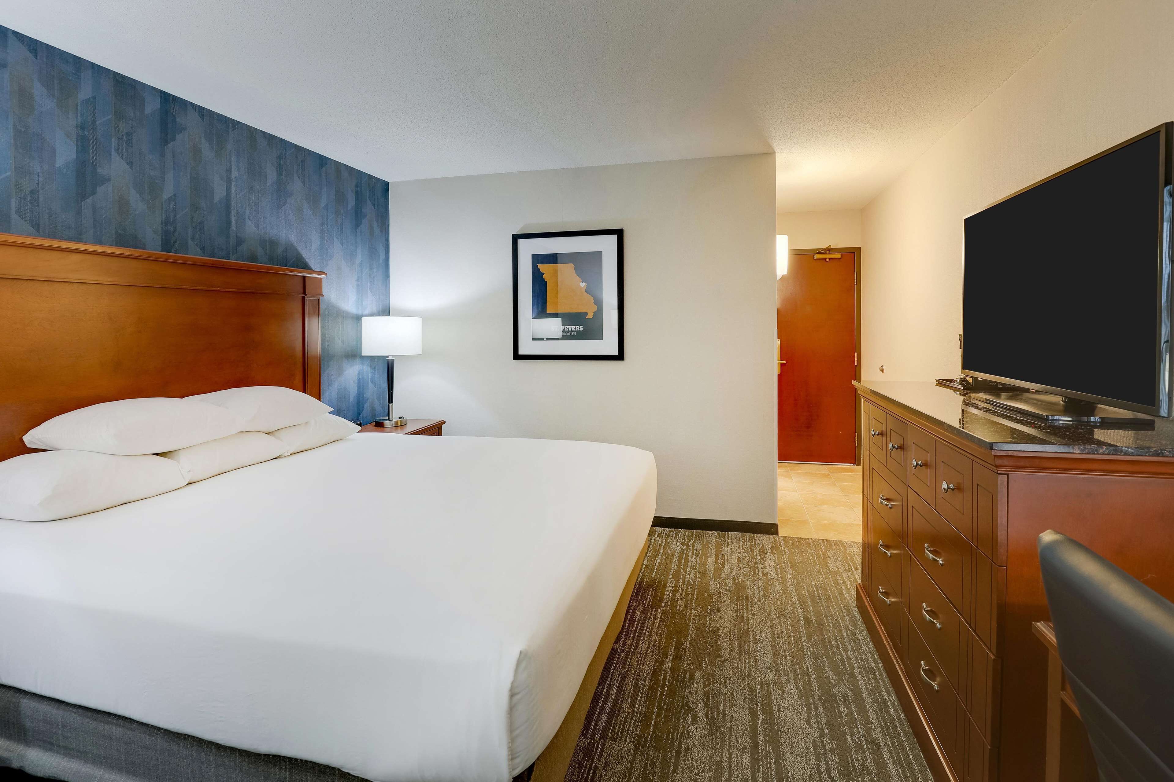 A hotel room with a large bed, a wooden headboard, a flat-screen TV, a dresser, and a framed map on the wall.