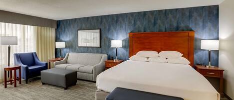 A hotel room with a large bed, two armchairs, a sofa, a small table, and a nightstand with lamps.