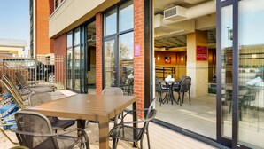 An outdoor patio area with a table and chairs, a glass door entrance, and a visible interior with a dining area. - Drury Inn & Suites St. Louis St. Peters (St. Peters)