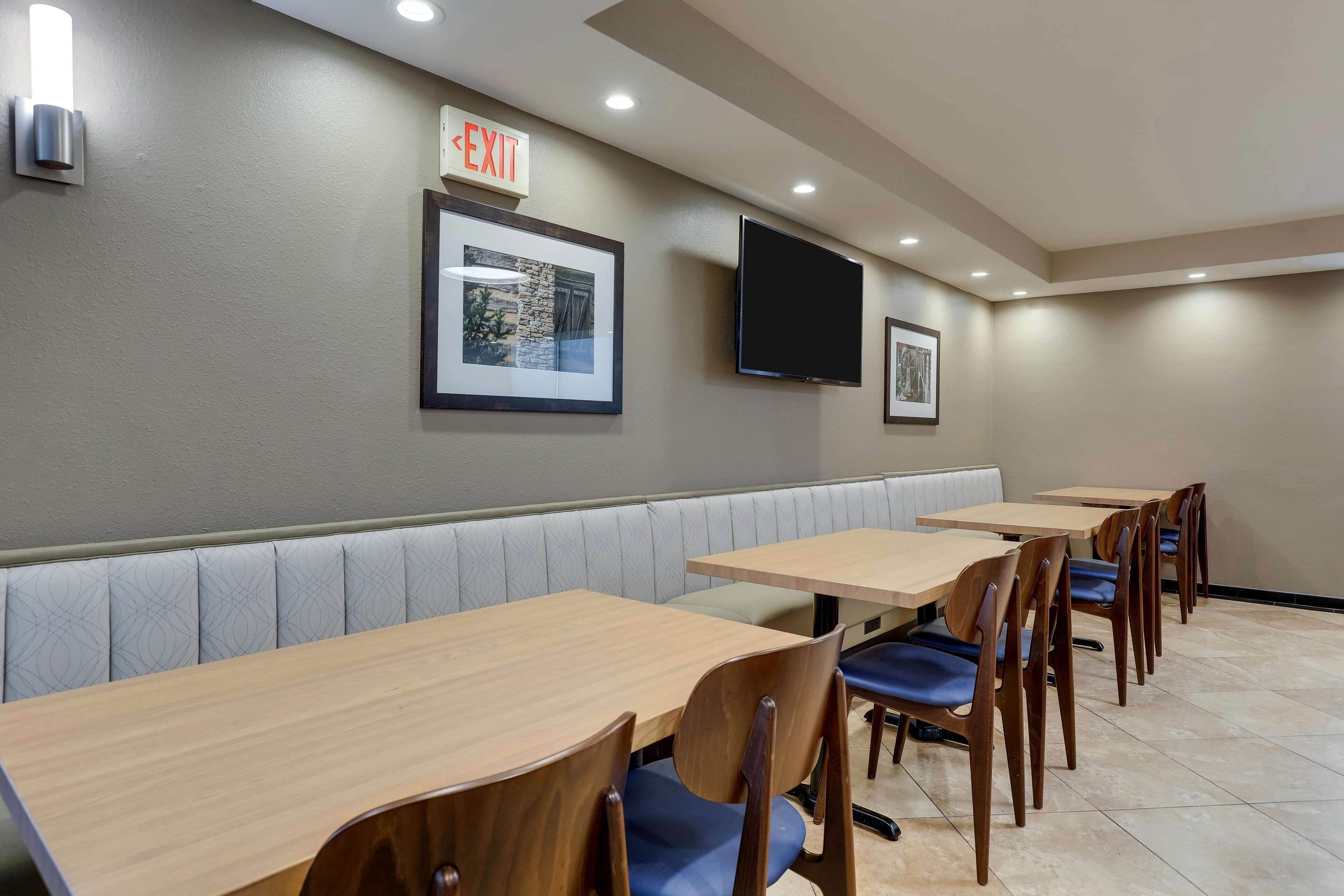 A restaurant with booths and tables, an exit sign, framed pictures, and a flat-screen TV on the wall.