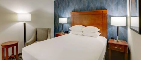 Ein Hotelzimmer mit einem großen Bett, zwei Nachttischen mit Lampen, einem Sessel und einem kleinen Hocker.