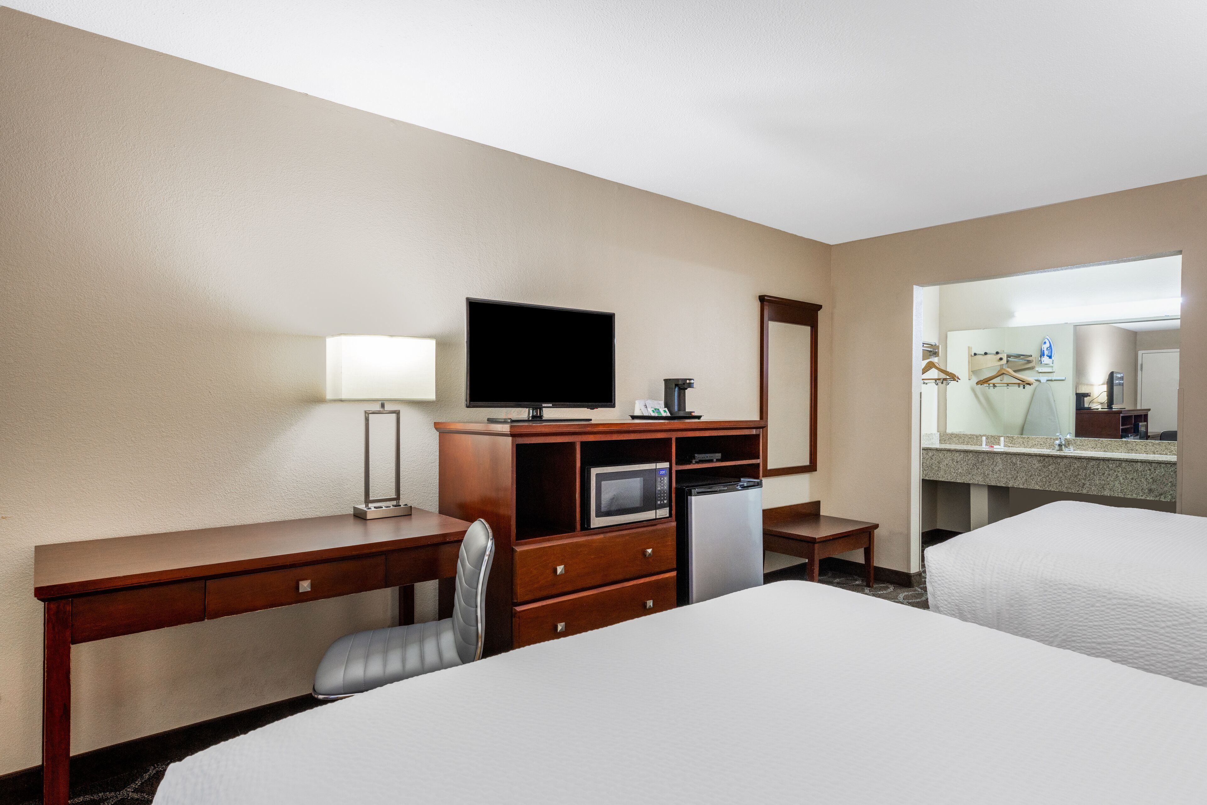 A hotel room with a bed, a desk with a television, a microwave, and a small table.