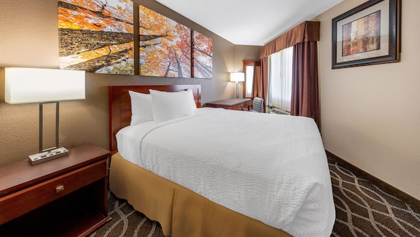 Une chambre d’hôtel avec un grand lit, un bureau, une chaise, une lampe et des œuvres d’art accrochées aux murs.