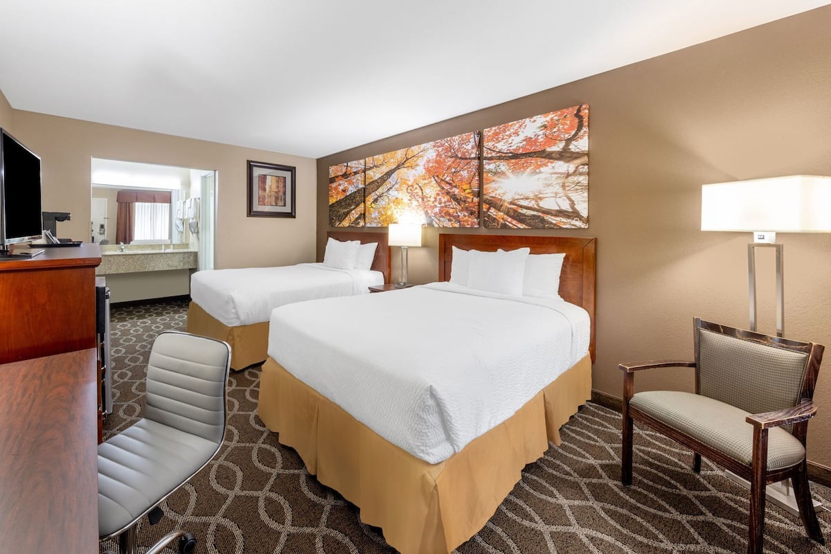 A hotel room with two beds, a desk, a chair, a TV, and a painting on the wall.