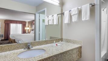 A hotel bathroom with a granite countertop sink, a mirror, and a towel rack with multiple white towels.