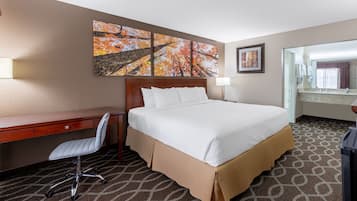A hotel room with a large bed, a desk, a chair, and a painting on the wall.