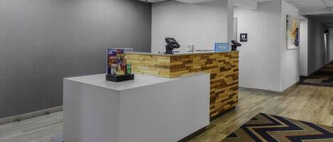Un espace d’accueil avec un comptoir de réception blanc, un mur d’accent en bois, un panneau bleu et un tapis à motifs.