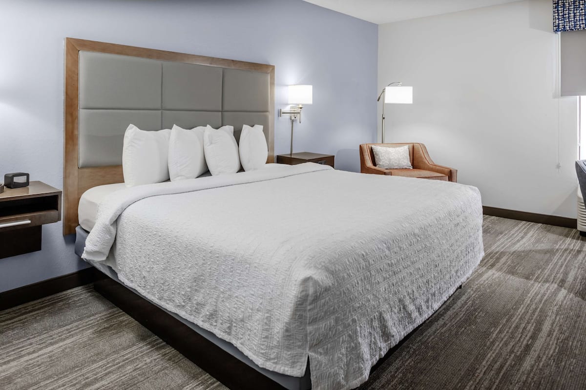 A hotel room with a large bed, a nightstand, a chair, and a lamp.
