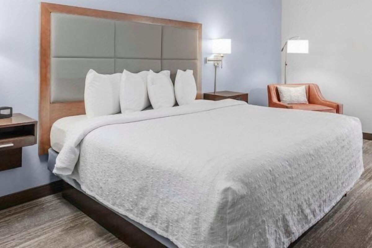 A hotel room with a large bed, a nightstand, a chair, and a lamp.