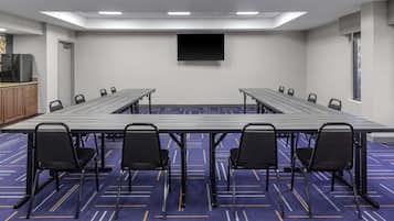 A conference room with a long table, chairs, a flat-screen TV, and a window.