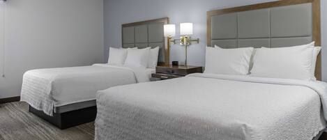 A hotel room with two beds, a nightstand with a lamp, and a carpeted floor.