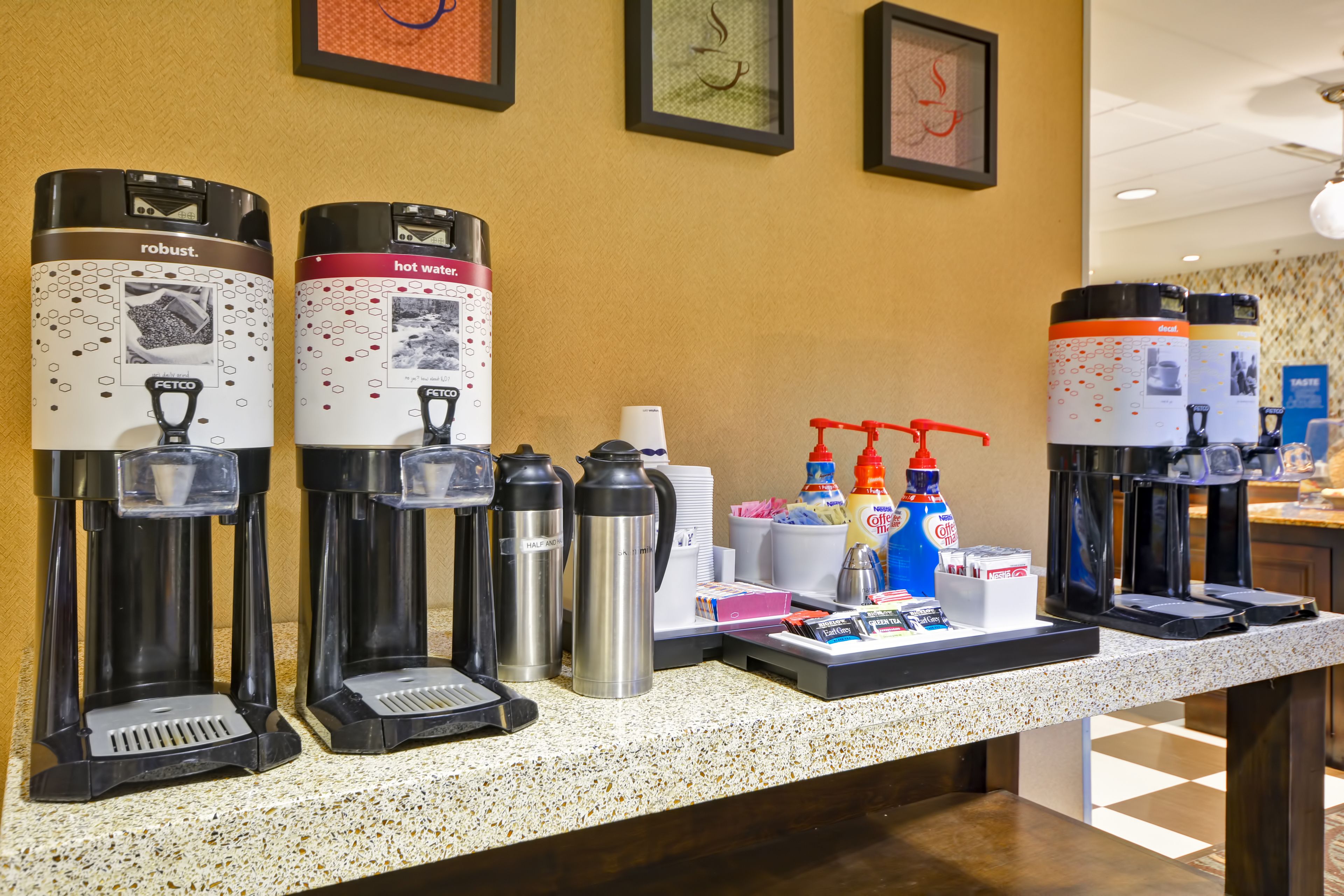 Una estación de café con varias cafeteras, tazas térmicas y condimentos.