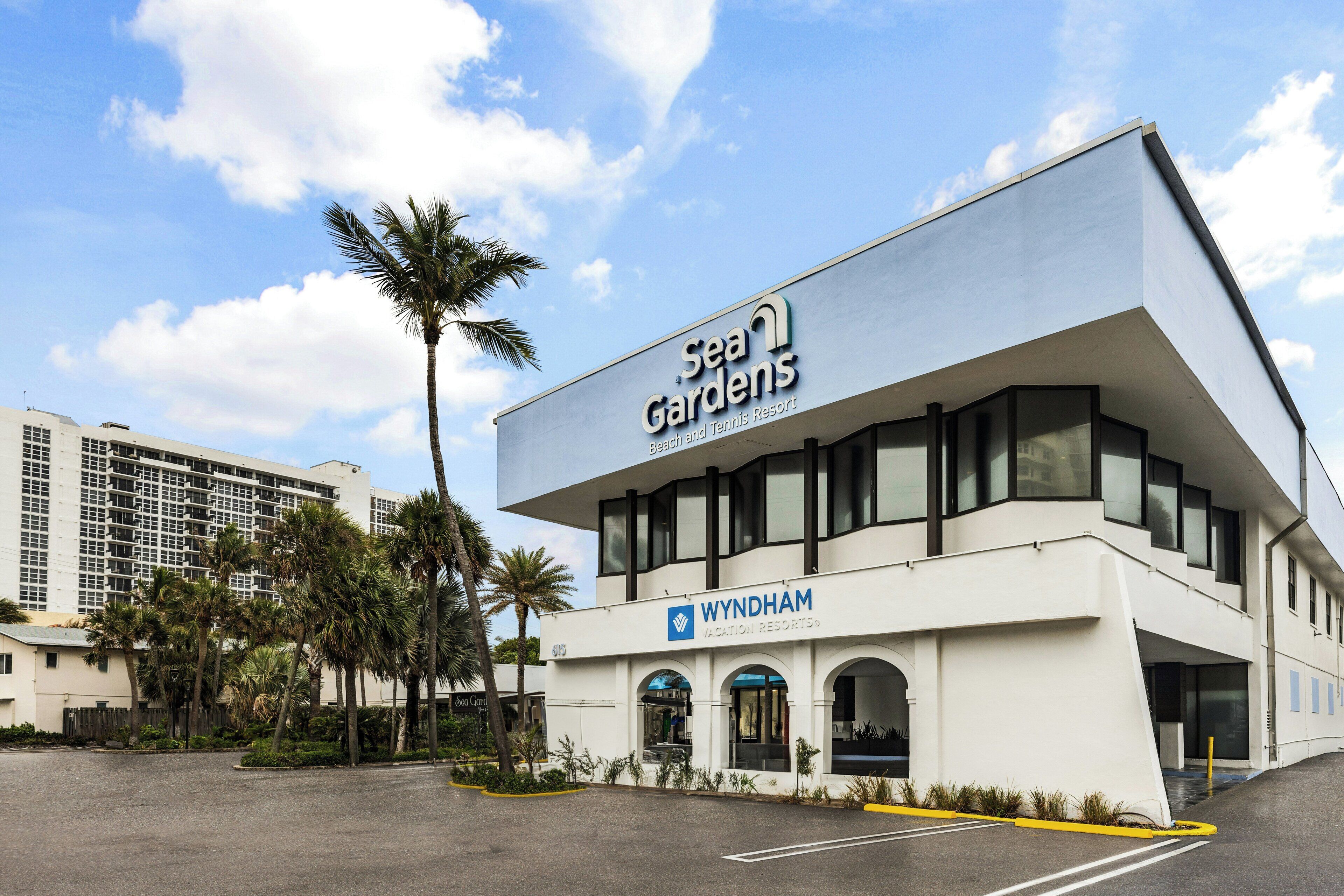 Un hôtel moderne, reconnaissable à son imposante enseigne « Sea Gardens », au logo « WYNDHAM » et à son parking agrémenté de palmiers.