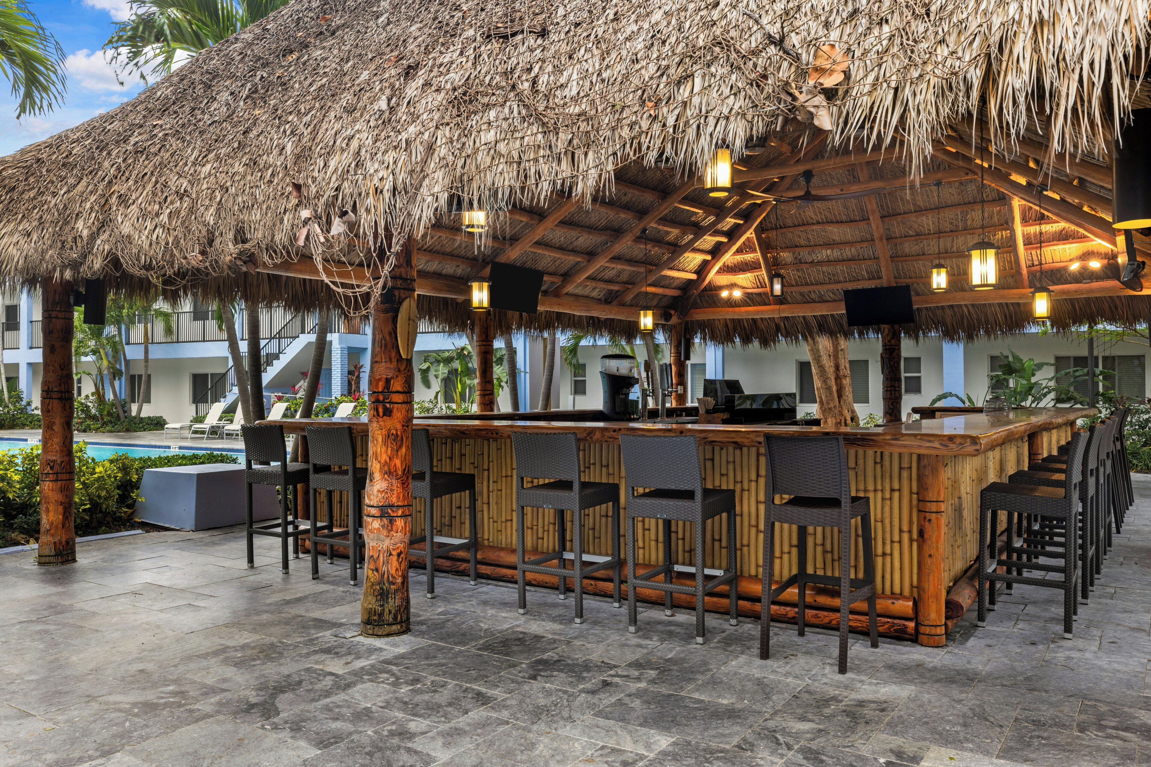 A bar area with a thatched roof, wooden bar counter, and multiple bar stools.