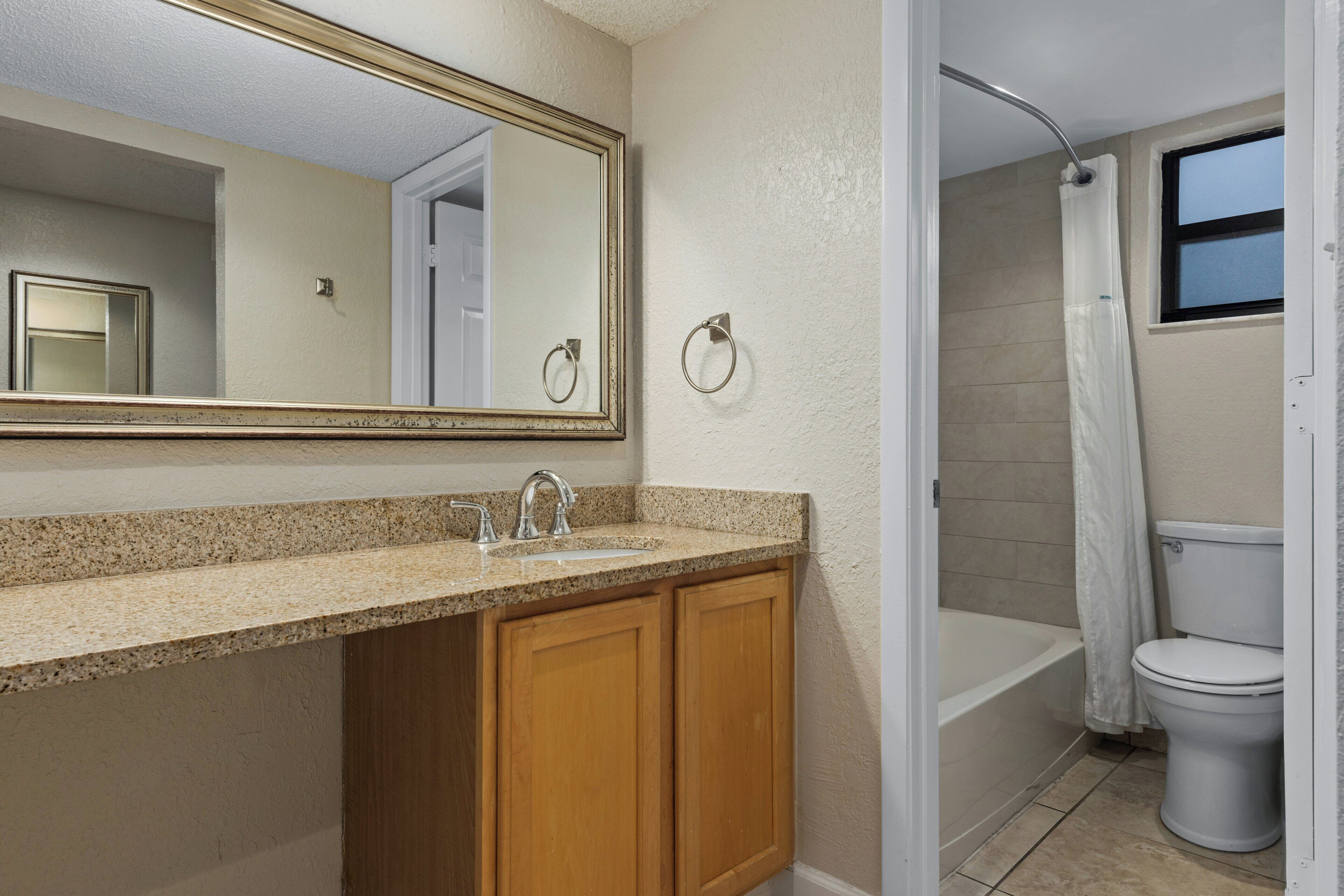 A bathroom with a sink, mirror, wooden cabinets, a shower, and a toilet.