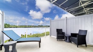 A covered outdoor seating area with a bench and two chairs, a white fence, and a view of greenery and water. - Hampton Inn Port Charlotte (Port Charlotte)