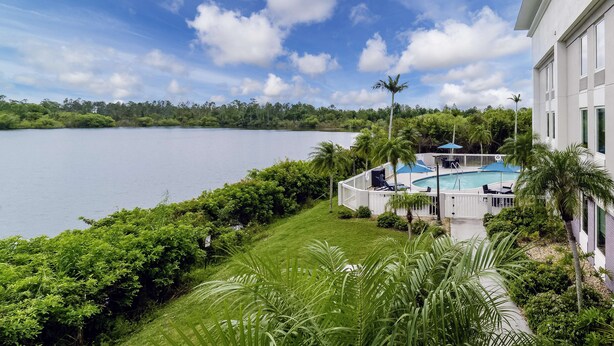 A pool area with a view of a lake, surrounded by lush greenery and palm trees. - Hampton Inn Port Charlotte (Port Charlotte)
