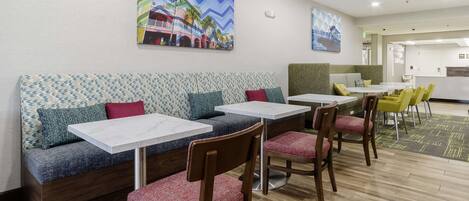 Un comedor moderno con sofá y mesas, una cocina al fondo y obras de arte en las paredes.
