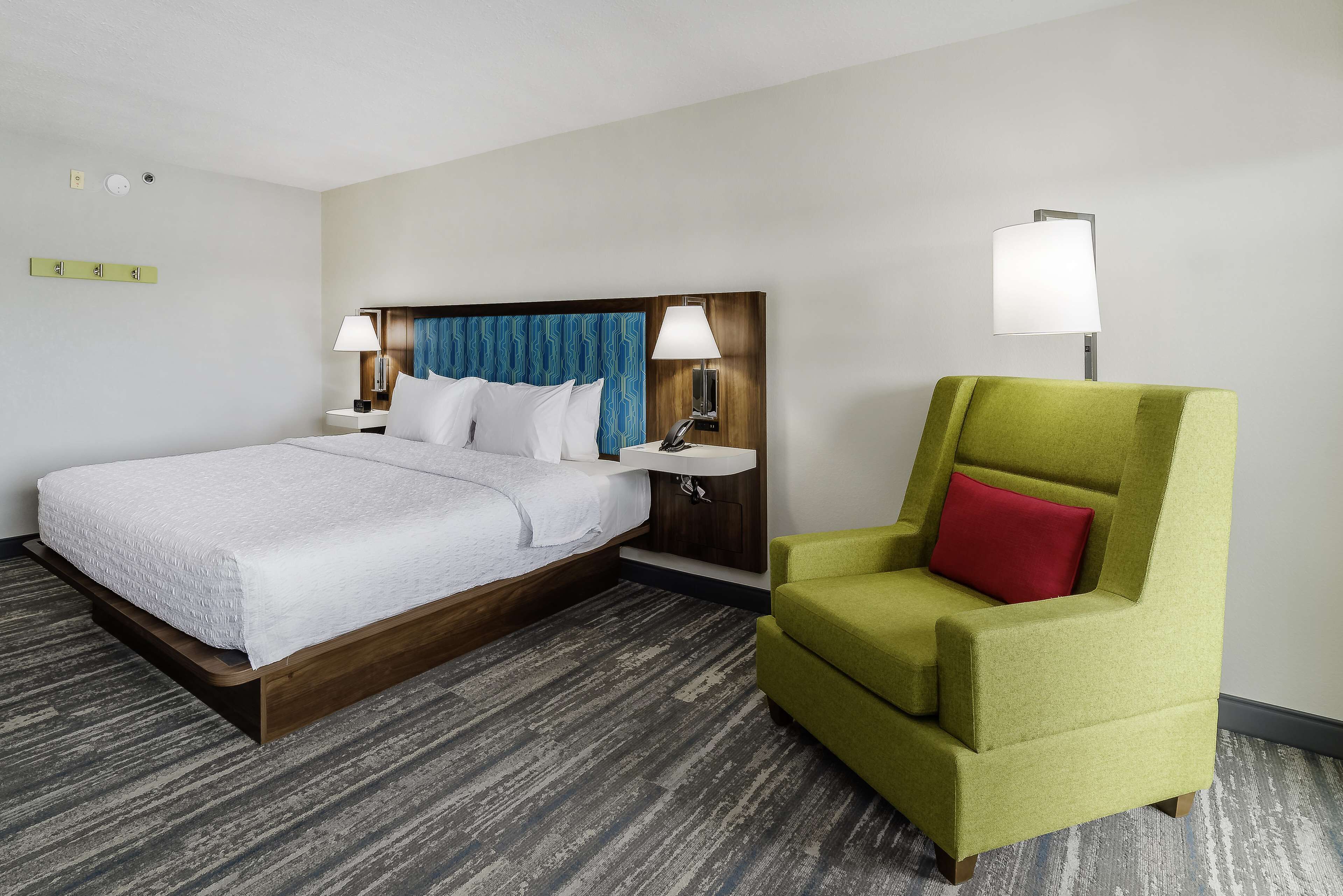 A hotel room with a bed, a nightstand, a lamp, and a green armchair.