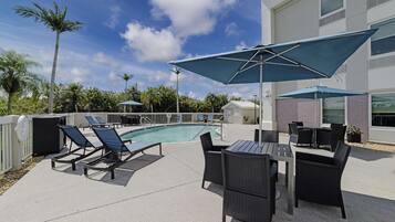A poolside area with lounge chairs, a table, and umbrellas.