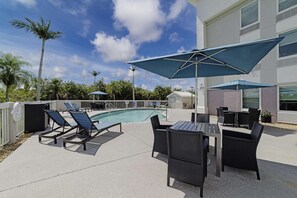 A poolside area with lounge chairs, a table, and umbrellas. - Hampton Inn Port Charlotte (Port Charlotte)