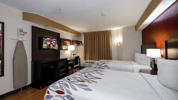 A hotel room with two beds, a TV, a desk with a chair, a lamp, and a window with curtains.