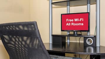 A computer desk with a monitor displaying 'Free Wi-Fi All Rooms' and a keyboard.