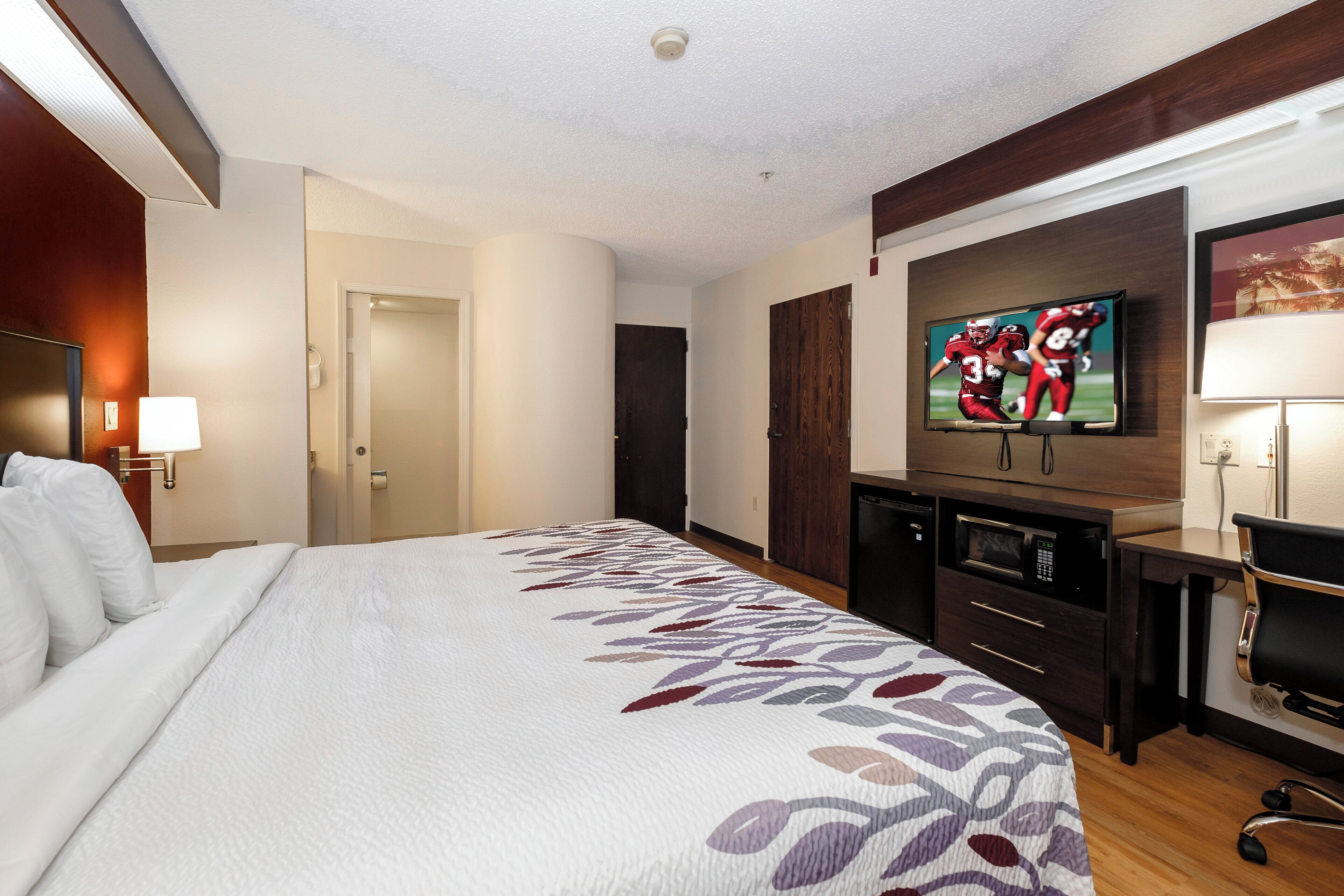 Habitación de hotel con cama, televisión, escritorio con silla y microondas.