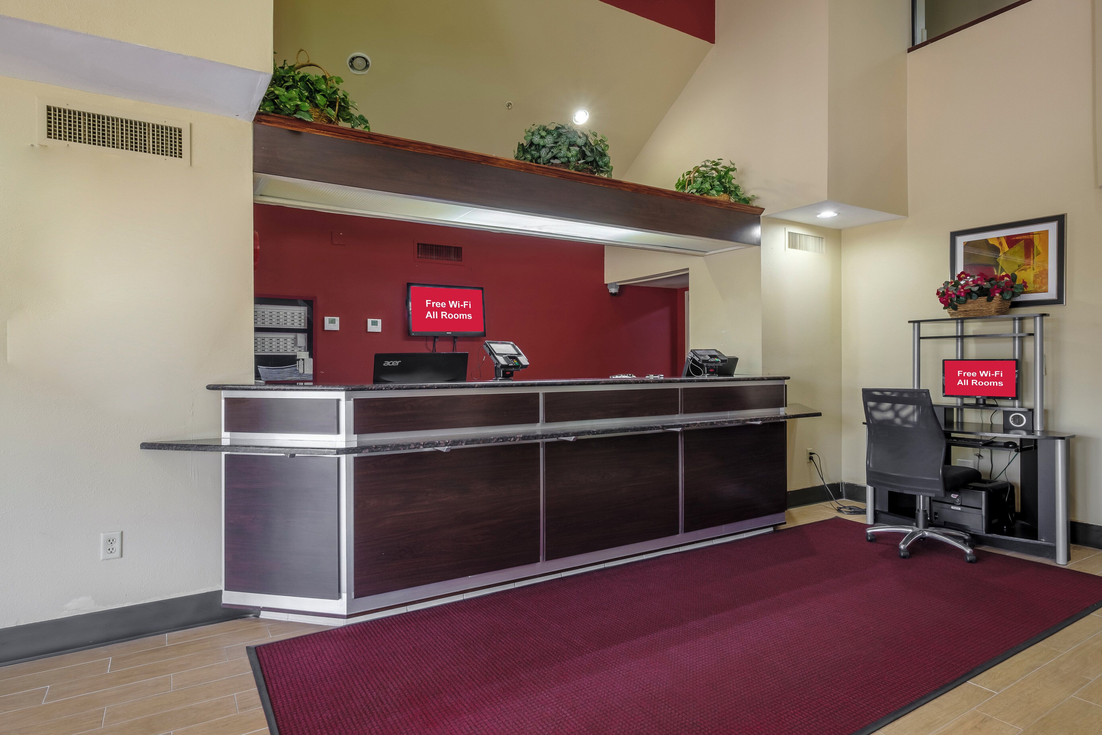 A reception desk with a red sign indicating free Wi-Fi in all rooms, a computer, a phone, and a small plant on top.