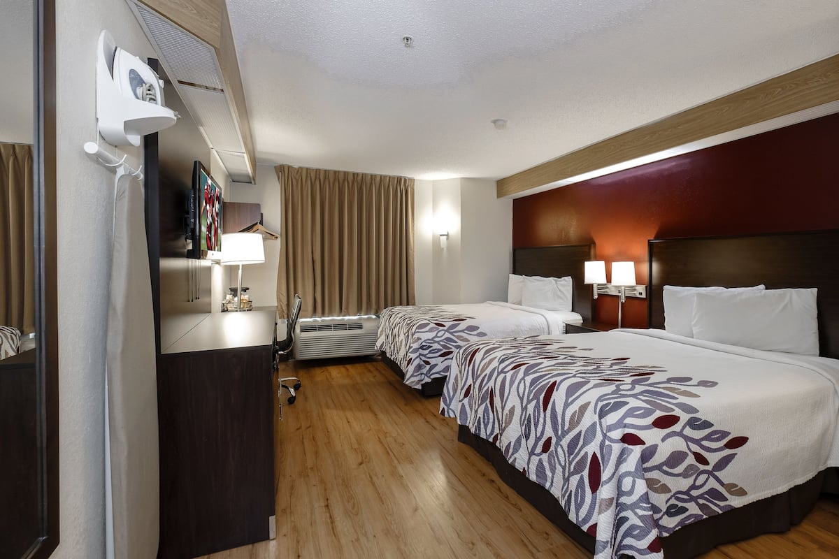 Camera d'albergo con due letti, una scrivania con una sedia, una TV a schermo piatto, un asciugacapelli, una lampada, una finestra con tende e un condizionatore d'aria.