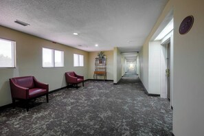 A hallway with carpeted flooring, two red chairs, a plant on a metal stand, and a door with a sign indicating room numbers. - Red Roof Inn Pensacola Fairgrounds (Pensacola)