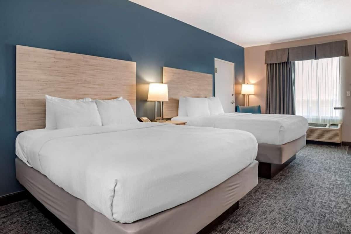 Ett hotellrum med två sängar, en mörkblå vägg och ett stort fönster med gardiner.