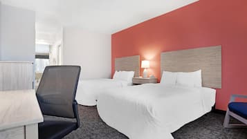 Una habitación de hotel con dos camas, un escritorio, una silla y una mesita de noche con lámpara.