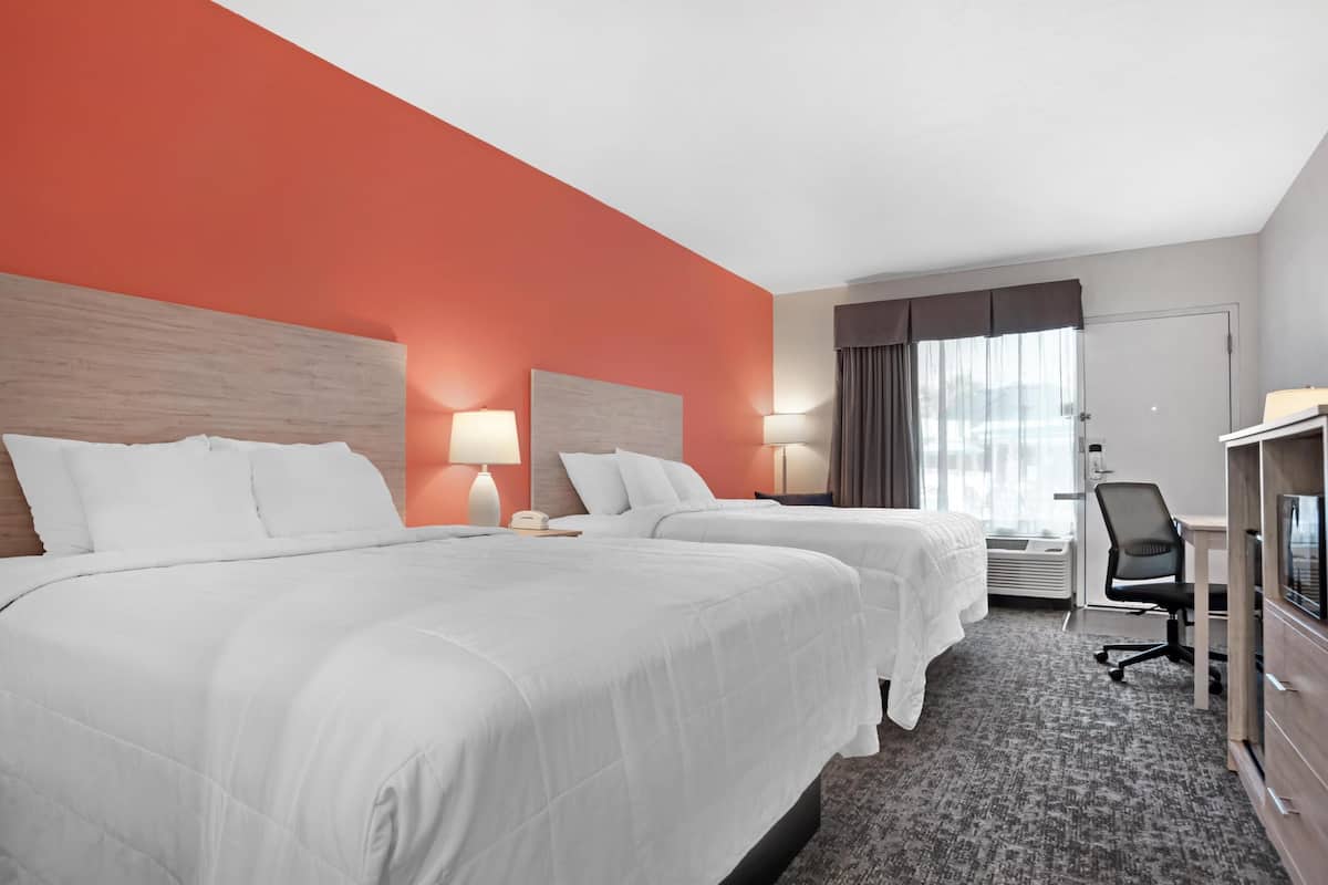 Ett hotellrum med två sängar, ett skrivbord, en stol och en tv.